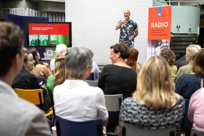 Dagvoorzitter op podium lacht en heeft interactie met aanwezigen