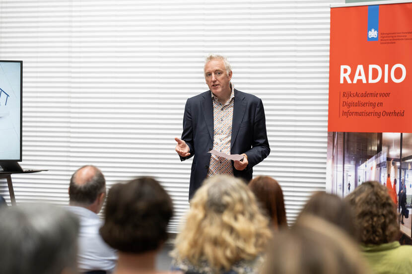 Directeur ODI op podium spreekt aanwezigen toe naast banner RADIO