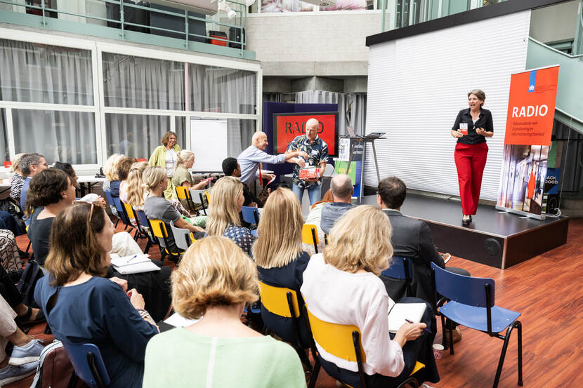 Marie Louise Borsje enthousiast op podium tijdens uitdelen van eerste RADIO Spaarkaarten door collega op de voorgrond